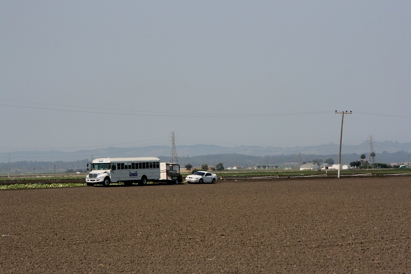 A field of farmland with vehicles in the background