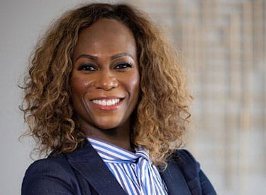 A professional headshot of Pamela Garmon Johnson wearing a navy blazer and blue and white striped blouse